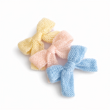 A cozy knit bow hair clip set featuring pastel-colored bows in soft shades of blue, pink, cream. Each bow is made from a textured knitted fabric, adding a charming and delicate touch to any hairstyle. Perfect for everyday wear or as a sweet accessory accent
