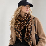 Model wearing a brown leopard print square scarf draped around her neck with a camel coat and black cap.