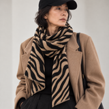 Model wearing a camel and black zebra print square scarf around her neck with a camel coat and black cap.