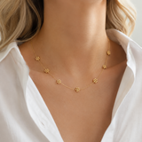 Gold necklace with small pendants on a person wearing a white shirt.