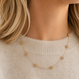 Gold necklace with small floral pendants on a beige sweater