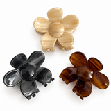 Three Daisy Claw Clips in marbled acetate — ivory, black, and amber — laid out together