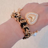 Gold-tone charm bracelet with a leopard-print scarf wrap, featuring dangling heart, cross, sun, and pearl-accented charms.