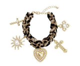 Gold-tone charm bracelet with a leopard-print scarf wrap, featuring dangling heart, cross, sun, and pearl-accented charms.