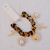 Gold-tone charm bracelet with a leopard-print scarf wrap, featuring dangling heart, cross, sun, and pearl-accented charms.