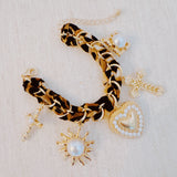 Gold-tone charm bracelet with a leopard-print scarf wrap, featuring dangling heart, cross, sun, and pearl-accented charms.