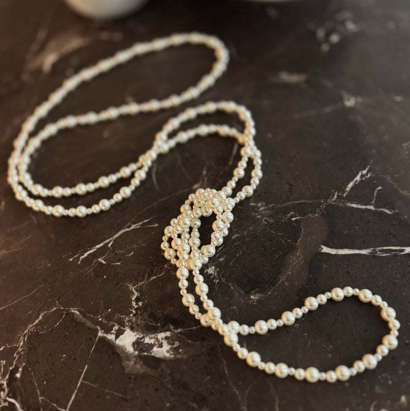 Long white beaded pearl necklace styled in gentle loops, ideal for layering or solo wear.