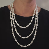 Long white beaded pearl necklace styled in gentle loops, ideal for layering or solo wear.