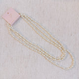 Long white beaded pearl necklace styled in gentle loops, ideal for layering or solo wear.