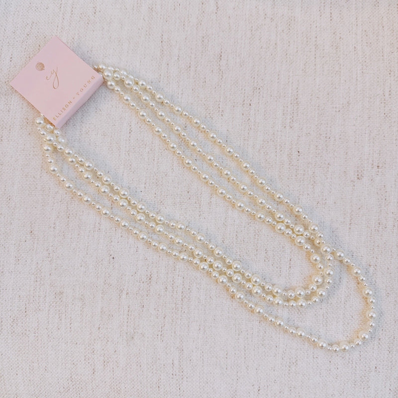 Long white beaded pearl necklace styled in gentle loops, ideal for layering or solo wear.