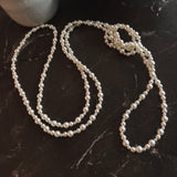 Long white beaded pearl necklace styled in gentle loops, ideal for layering or solo wear.