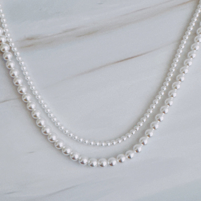 Set of two versatile pearl necklaces featuring luminous pearls in varying sizes, designed with magnetic clasps for easy wear and styling; can be worn individually or linked together for a longer layered look.