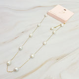 Pearl necklace on a marble surface with a pink card in the background