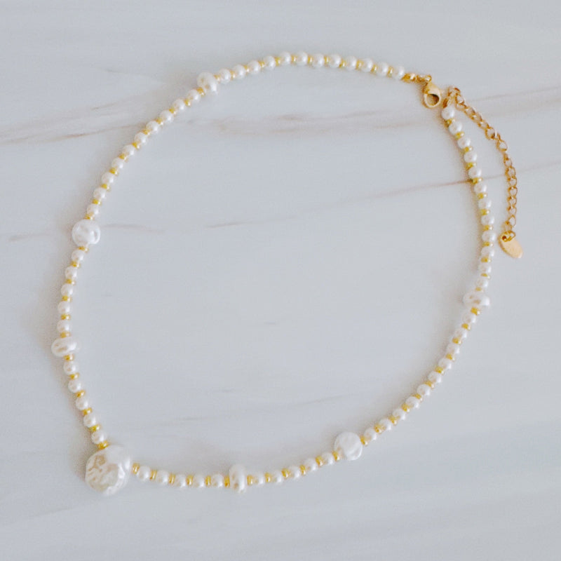 Gold-tone chain necklace featuring a mix of small polished pearls and irregular freshwater-style pearls, finished with an adjustable clasp closure.