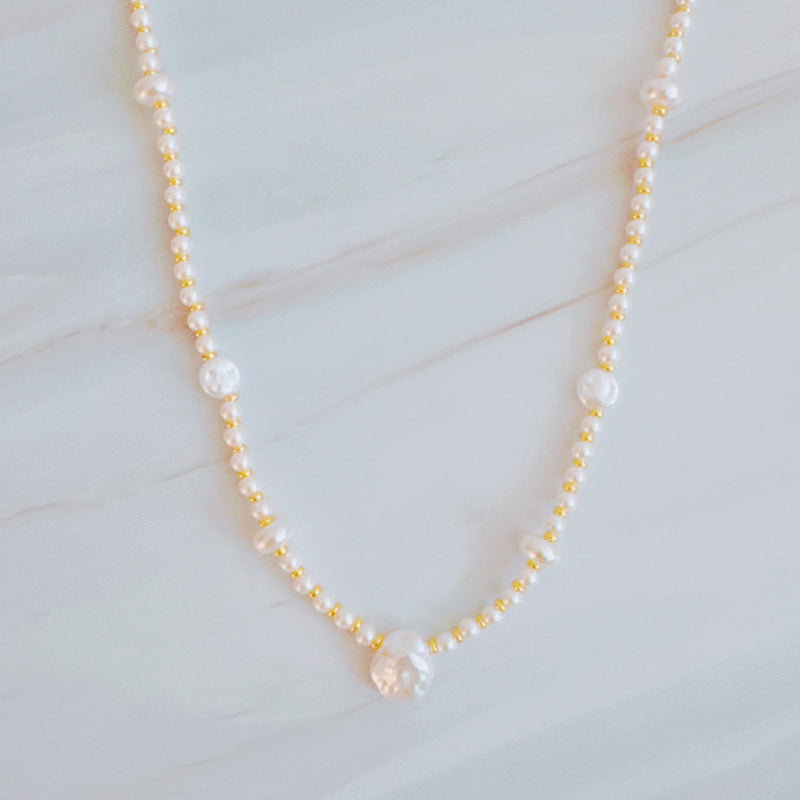 Gold-tone chain necklace featuring a mix of small polished pearls and irregular freshwater-style pearls, finished with an adjustable clasp closure.