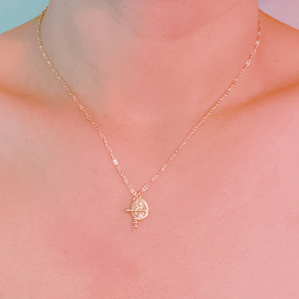Delicate gold-tone chain necklace featuring two charms – a textured mini cross and an oval saint medallion, blending faith and fashion effortlessly