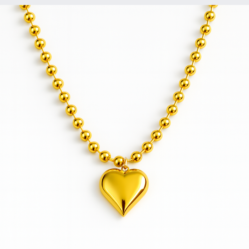 Gold-toned necklace featuring a chunky beaded chain and a bold puffed heart pendant, creating a striking statement piece with vintage flair.