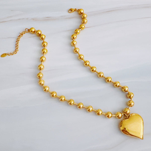 Gold-toned necklace featuring a chunky beaded chain and a bold puffed heart pendant, creating a striking statement piece with vintage flair.