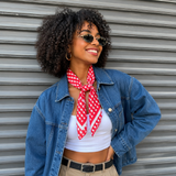Woman wearing a denim jacket, white top, and red checkered scarf against a metal shutter background