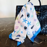 Seashell patterned scarf draped over a black handbag on a marble surface