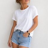 a black rope bracelet with gold heart charm, wearing it on the wrist, wearing white shirt and jean shorts