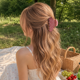 Woman with long wavy hair wearing a checkered hair clip, sitting outdoors with a picnic basket and food.