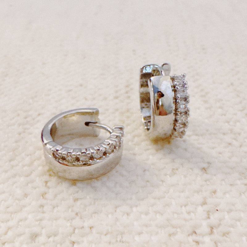 Contoured silver-tone huggie earrings featuring a sleek sculpted shape with a subtle strip of sparkling stones along one edge for a hint of glam.