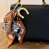 Chic bag charm featuring a flowing printed scarf tied to a gold-tone chain with assorted golden charms for a luxe, fashion-forward accessory