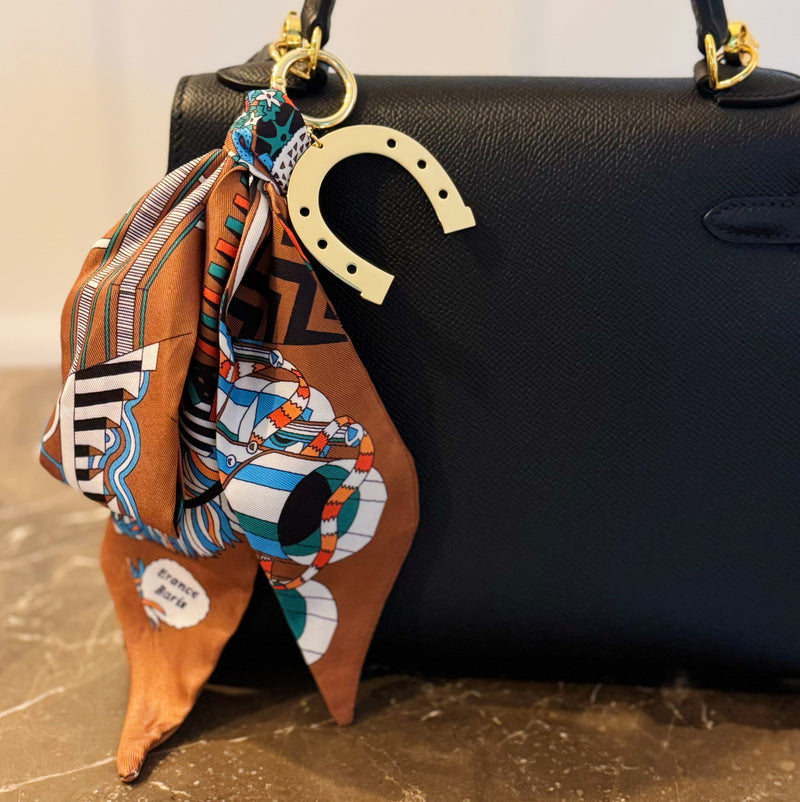 Chic bag charm featuring a flowing printed scarf tied to a gold-tone chain with assorted golden charms for a luxe, fashion-forward accessory