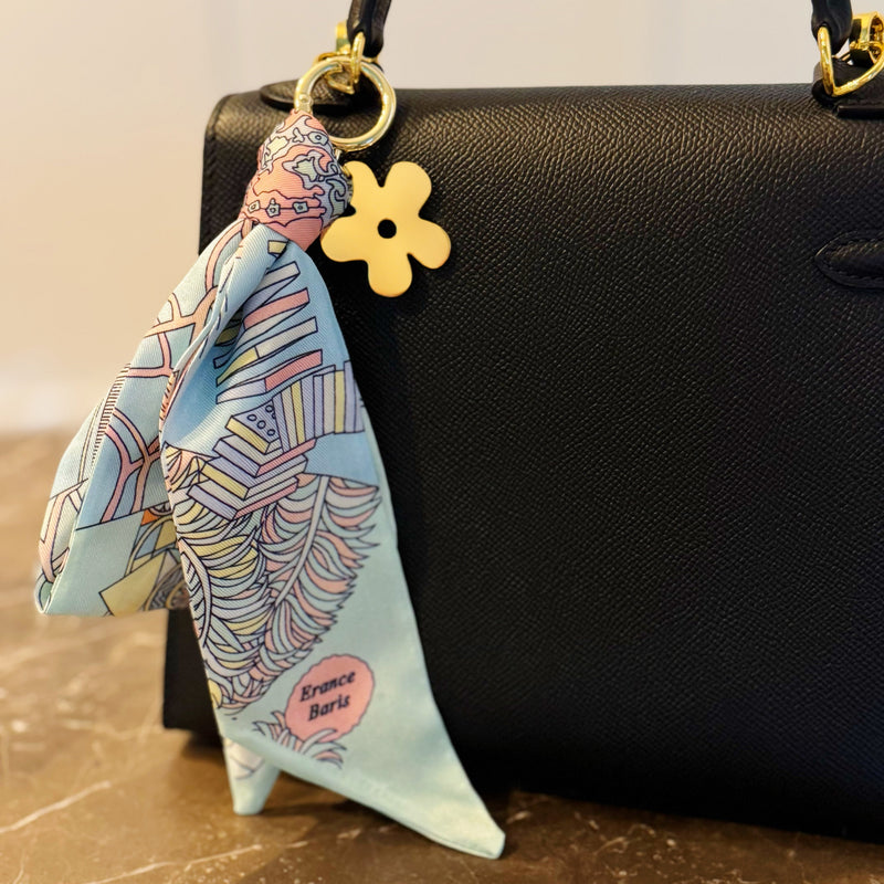 Chic bag charm featuring a flowing printed scarf tied to a gold-tone chain with assorted golden charms for a luxe, fashion-forward accessory