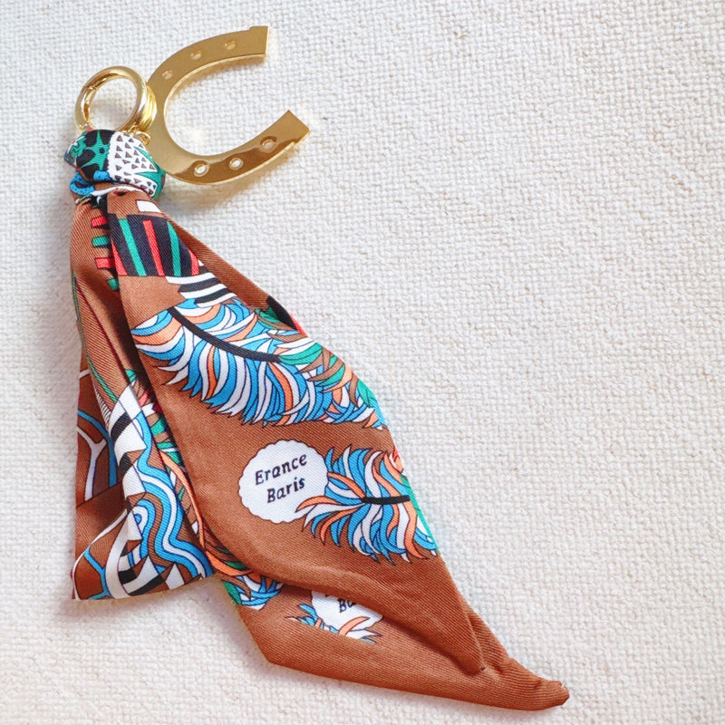 Chic bag charm featuring a flowing printed scarf tied to a gold-tone chain with assorted golden charms for a luxe, fashion-forward accessory