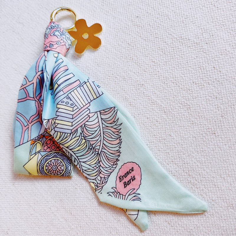 Chic bag charm featuring a flowing printed scarf tied to a gold-tone chain with assorted golden charms for a luxe, fashion-forward accessory