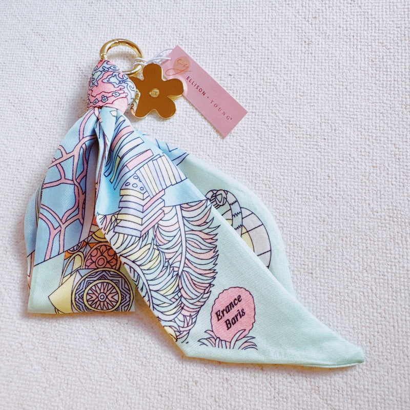 Chic bag charm featuring a flowing printed scarf tied to a gold-tone chain with assorted golden charms for a luxe, fashion-forward accessory