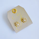 Gold-tone floral stud earrings featuring a luminous pearl center surrounded by petal-shaped sections adorned with sparkling crystals. The earrings create a radiant, feminine look that blends timeless charm with elegant shine.