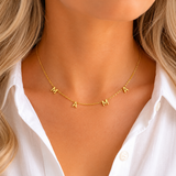 Gold necklace with 'MAMA' letters on a person wearing a white shirt.