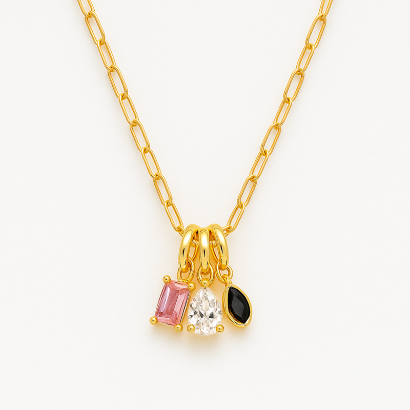 Close-up of a gold paperclip chain necklace featuring an eclectic mix of dangling gem-shaped charms in various cuts and colors, the stones clustered at the center.