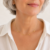 Woman wearing a gold necklace with small pendants on a plain background