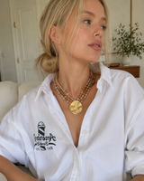 Woman wearing a white shirt with a logo and a necklace in an indoor setting