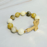 Bracelet with beige and white beads and a gold ribbon charm on a light gray background