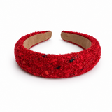 A wide, chunky headband covered in textured red sequins and glitter, with a visible tan cardboard inner band, photographed on a clean white background.