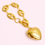 Gold chain bracelet with a heart-shaped pendant on a light pink background