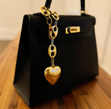 Black handbag with a gold heart-shaped charm on a wooden surface