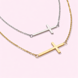 Two cross necklaces, one gold and one silver, on a light pink background.
