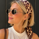 Woman wearing sunglasses and a leopard print headscarf against a dark background