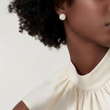 Elegant stud earrings featuring a stone encircled by small sparkling crystals, all set in a polished gold frame. The cushion-cut center gem catches the light beautifully, creating a timeless and sophisticated look.