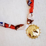 Elegant scarf necklace featuring a bold medallion pendant and luxe printed fabric intertwined with a chain, combining statement style with wearable versatility.