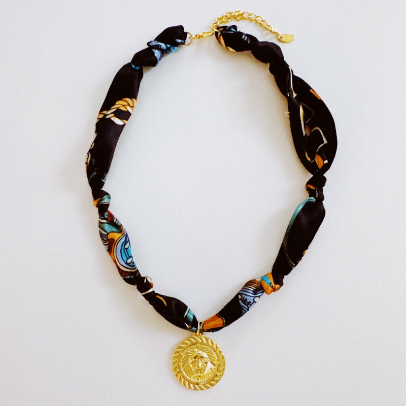 Elegant scarf necklace featuring a bold medallion pendant and luxe printed fabric intertwined with a chain, combining statement style with wearable versatility.