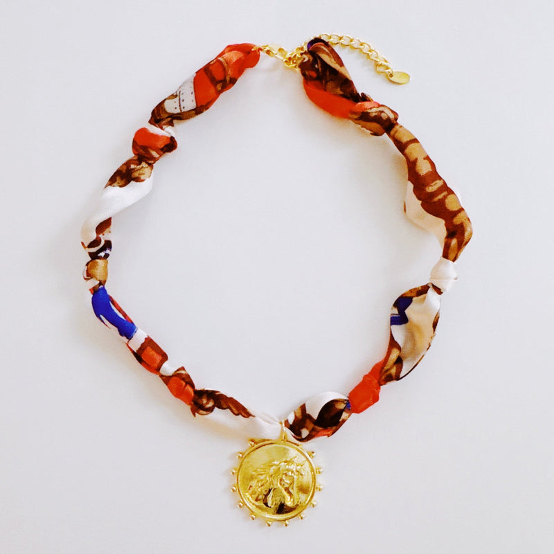 Elegant scarf necklace featuring a bold medallion pendant and luxe printed fabric intertwined with a chain, combining statement style with wearable versatility.