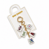 A gold-tone bag charm keychain featuring four white square tiles with colorful illustrations of mahjong tiles (2, 3, 4, and 10), displayed on a white card labeled 'BAG CHARM'.