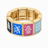 A gold-plated stretch bracelet featuring four square panels with colorful enameled faces: black with a white pagoda, blue with a white bird and the number 1, pink with a white wheel and the number 2, and light blue with white grid patterns.
